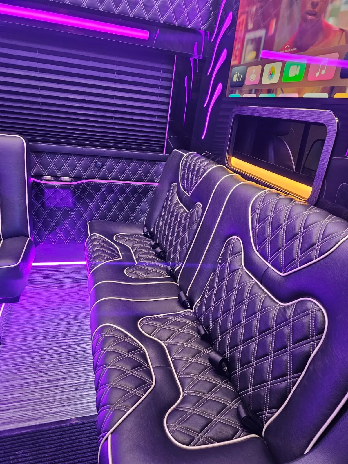 Limo Sprinter lounge seating beside an entertainment screen and purple ambient lighting